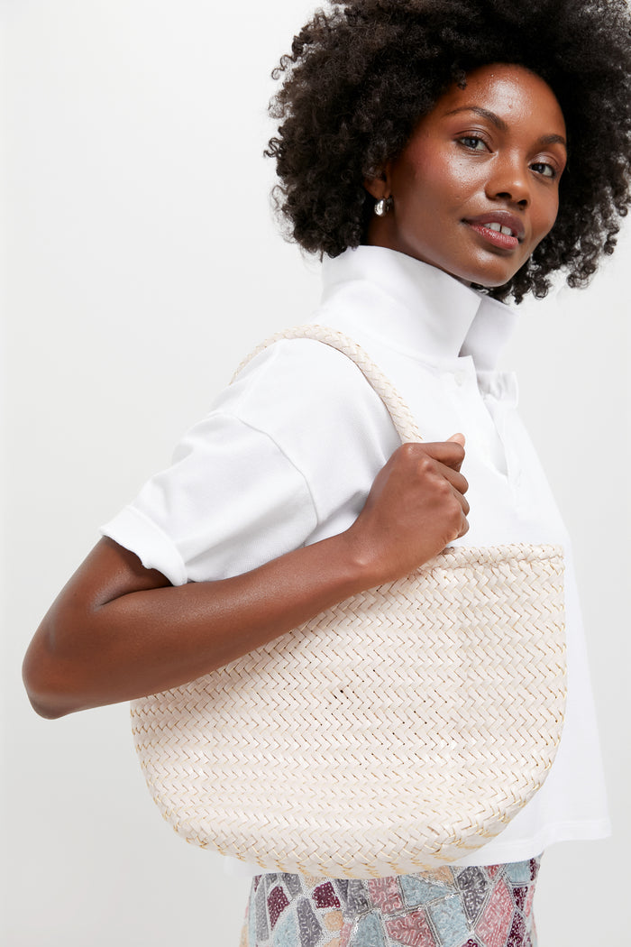 Person carries Sand Small Grace Basket, a classic, high-end tote with braided handles, effortlessly pairing with a white polo and patterned skirt for a fun, versatile look.
