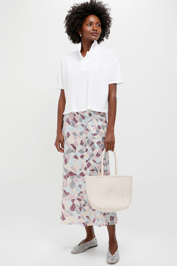 Woman holding Sand Small Grace Basket, exuding classic, effortless style. Boxy white polo top, pastel mosaic skirt, grey flats enhance the high-end, fun look.