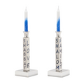 The Shabbat Candlestick Set/2 by Inspired Generations features two silver holders, each with blue-and-white candles and blue "SHABBAT" and "SHALOM" inscriptions—ideal for a meaningful, welcoming table setting.