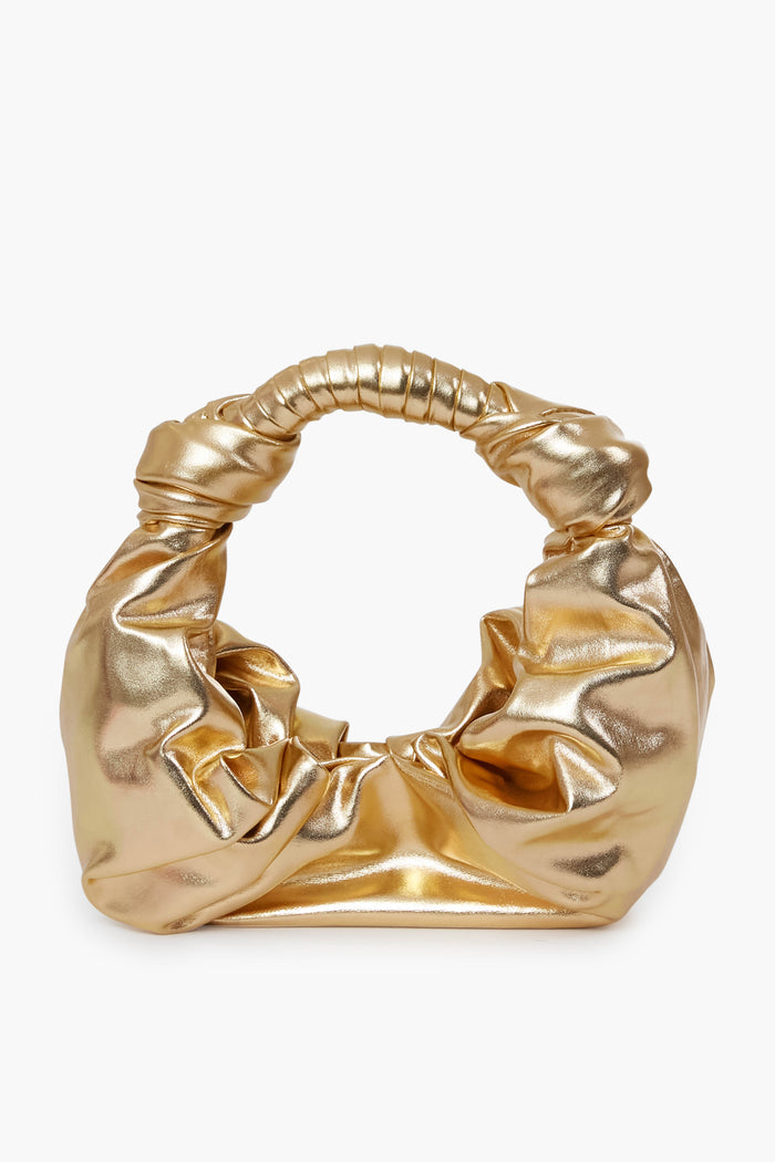 A gold metallic faux leather bag by Simon Miller features a gathered, ruched design with a wrapped handle—ideal as a statement purse.