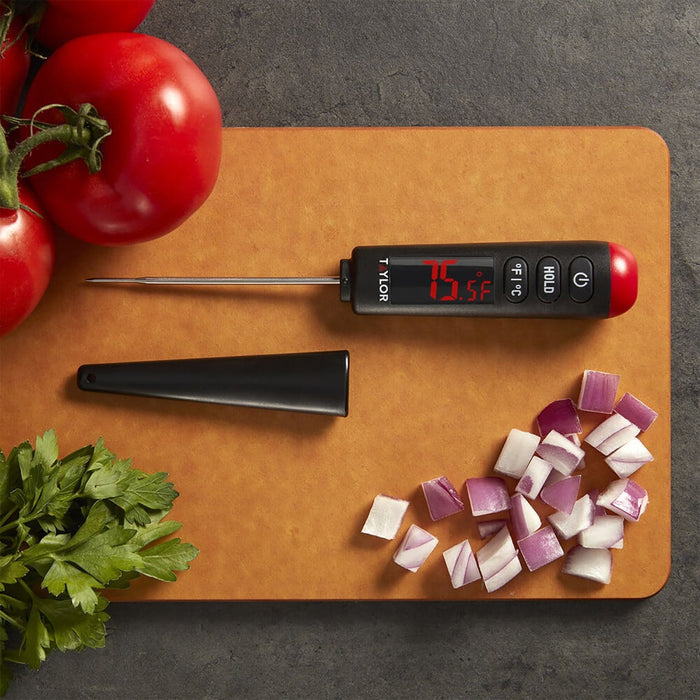 Digital thermometer with red LED display showing 75.5°F on a cutting board beside chopped vegetables
