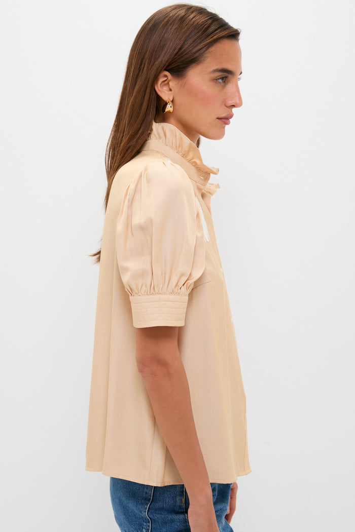 Woman in Tan & Cream Embroidery Louisa Blouse with ruffle collar and puff sleeves, paired with jeans, showcasing a classic, effortless high-end style.