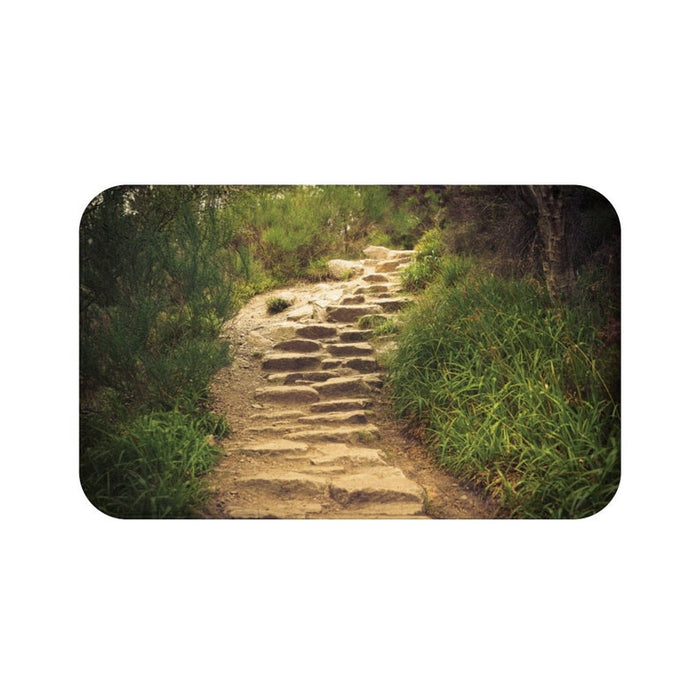 The image on this memory foam floor mat is of a stone pathway leading down a trail with tall grasses and trees on either side. The image has been brightened to make the pathway's dirt and stone steps pop out.