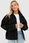 A woman with long blonde hair wears a Nude Lucy oversized vintage black stone wash denim jacket over a white ribbed sweater and light blue jeans.