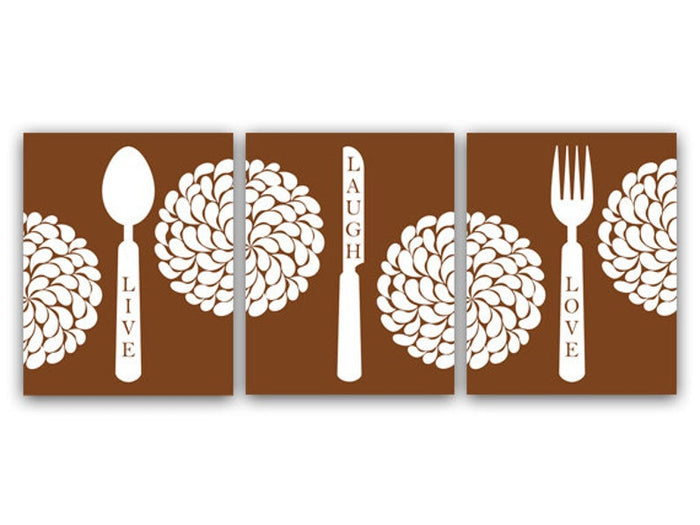A set of three brown and white kitchen-themed art prints, with one depicting a spoon and the word 'LIVE', another a fork and 'LAUGH', and the last a knife and 'LOVE'. The words are vertical along the handle of each utensil. The background is brown. A circular, floral petal design brings the three panels together with a flower split across the left and center panels, and a flower split across the center and right panels.