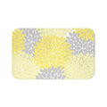 A rectangular memory foam mat with an abstract, yellow, light yellow, and gray floral burst pattern against a white background, and with an anti-slip backing.